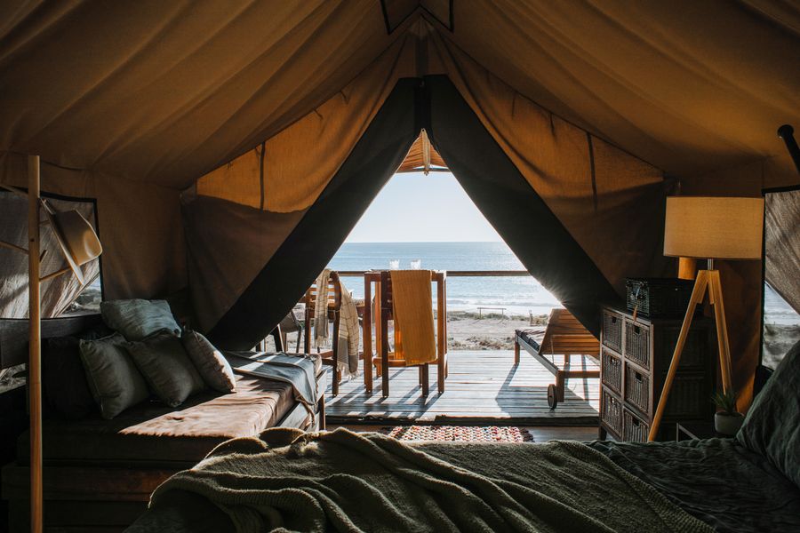 Interior of a safari-style glamping tent opening onto a deck and sea